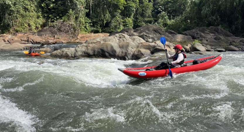 A person wearing safety gear paddles a red watercraft through whitewater